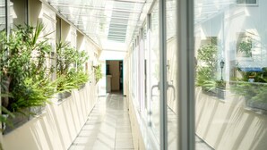 A corridor with glass walls, potted plants, and a tiled floor.
