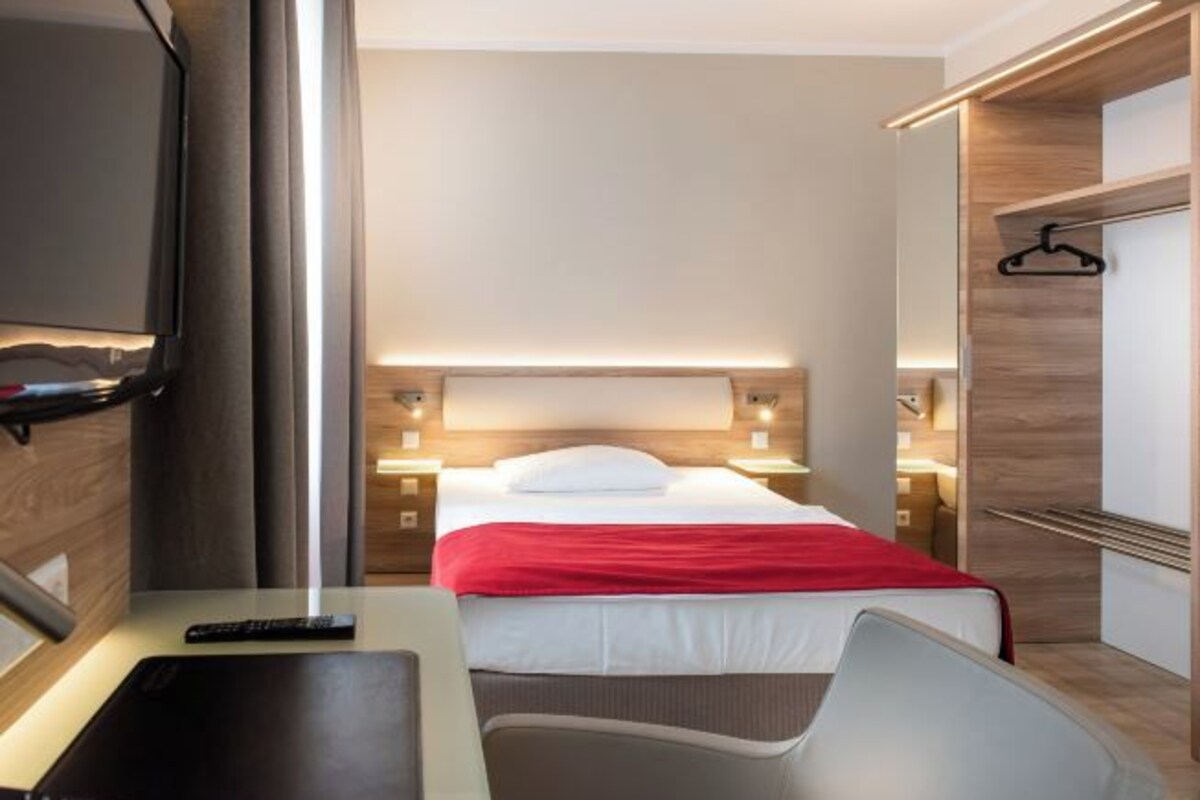 A hotel room with a bed, bedside tables, a desk, and a TV.