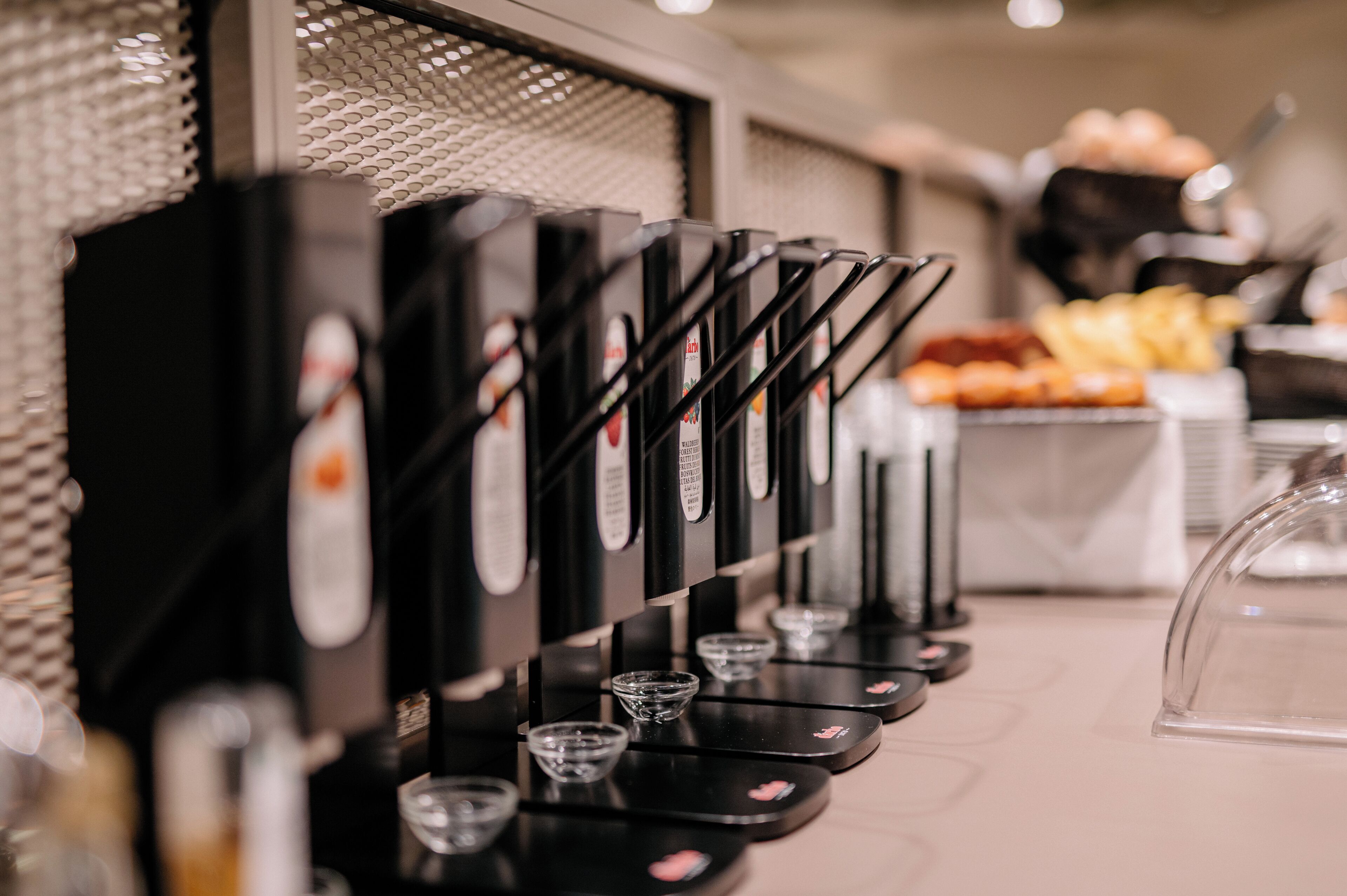 Máquina de café com vários dispensadores e pequenas chávenas de vidro.