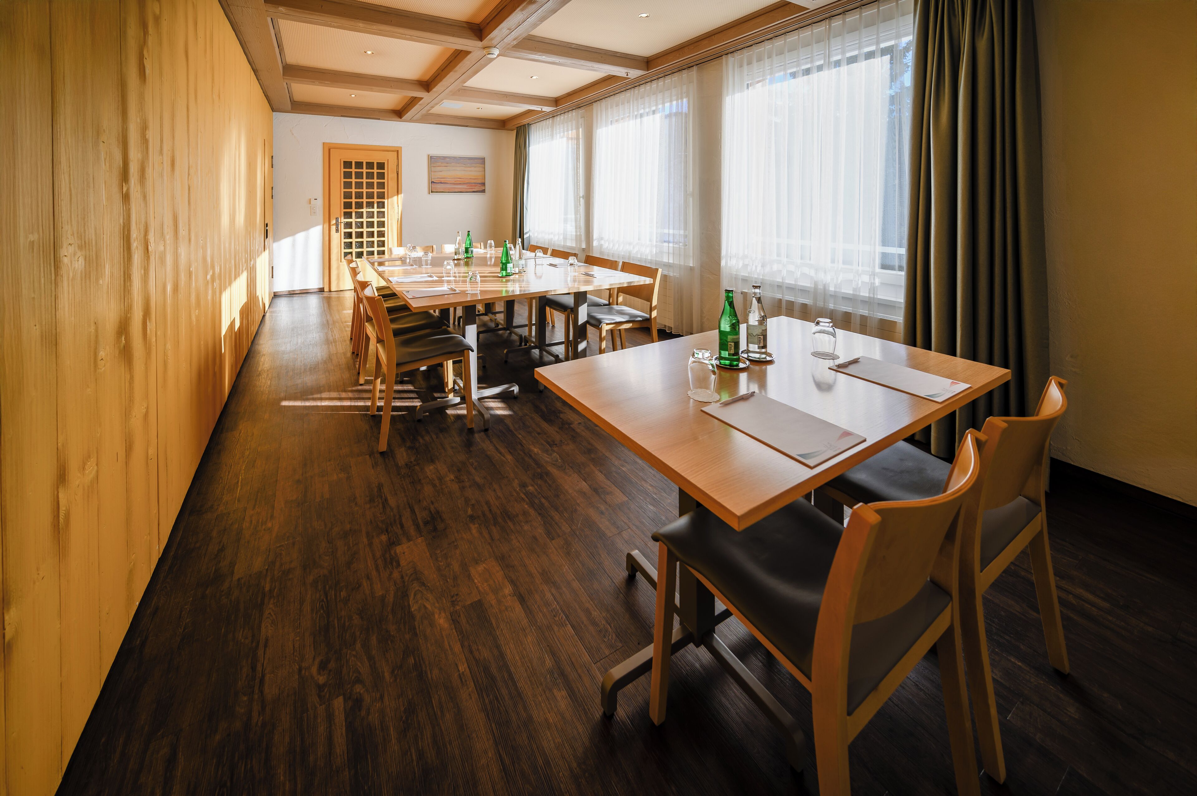A conference room with a long table, chairs, and a wooden floor.