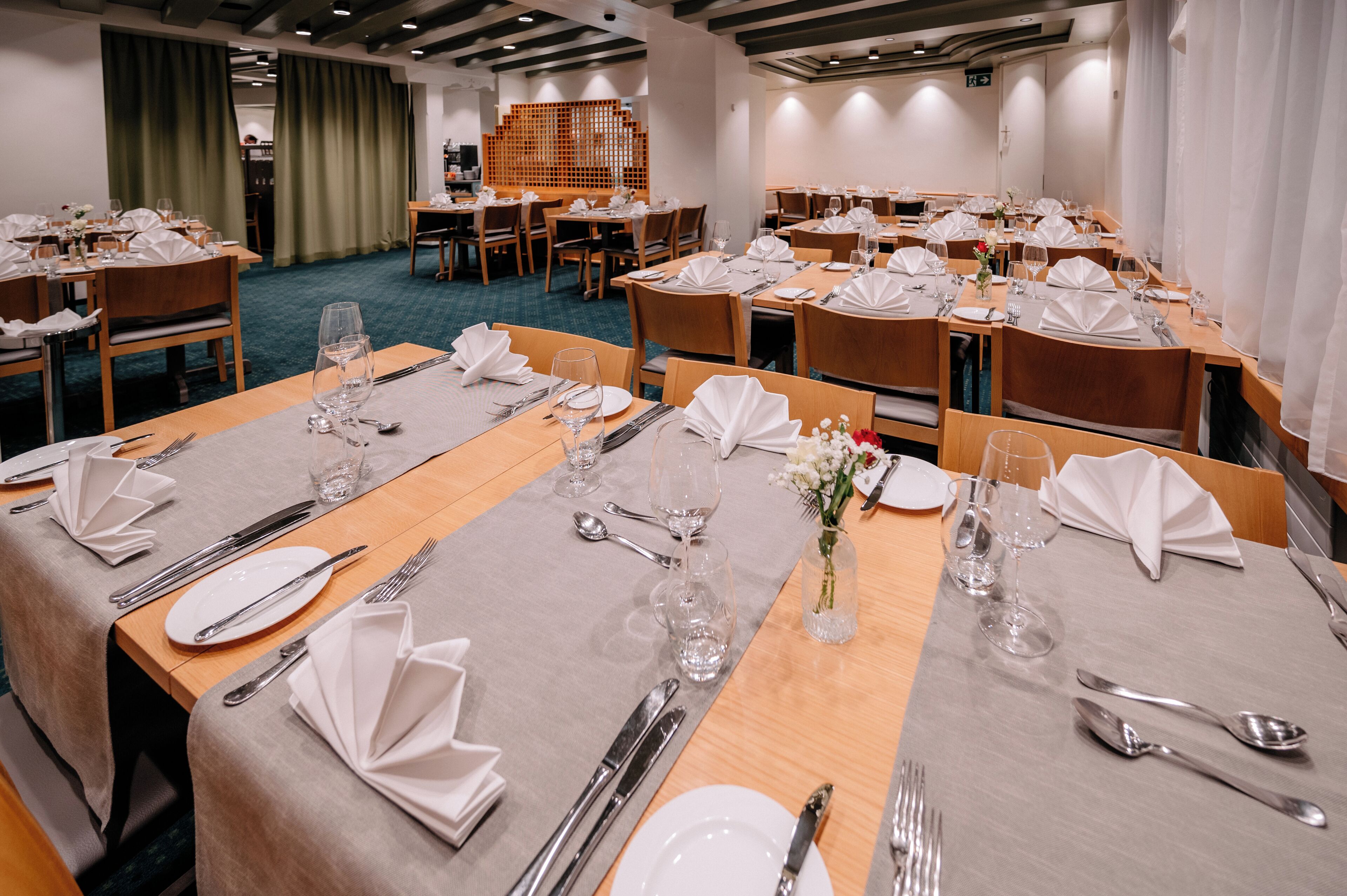 Une salle de conférence équipée de plusieurs tables dressées pour un repas, avec assiettes, couverts et verres.