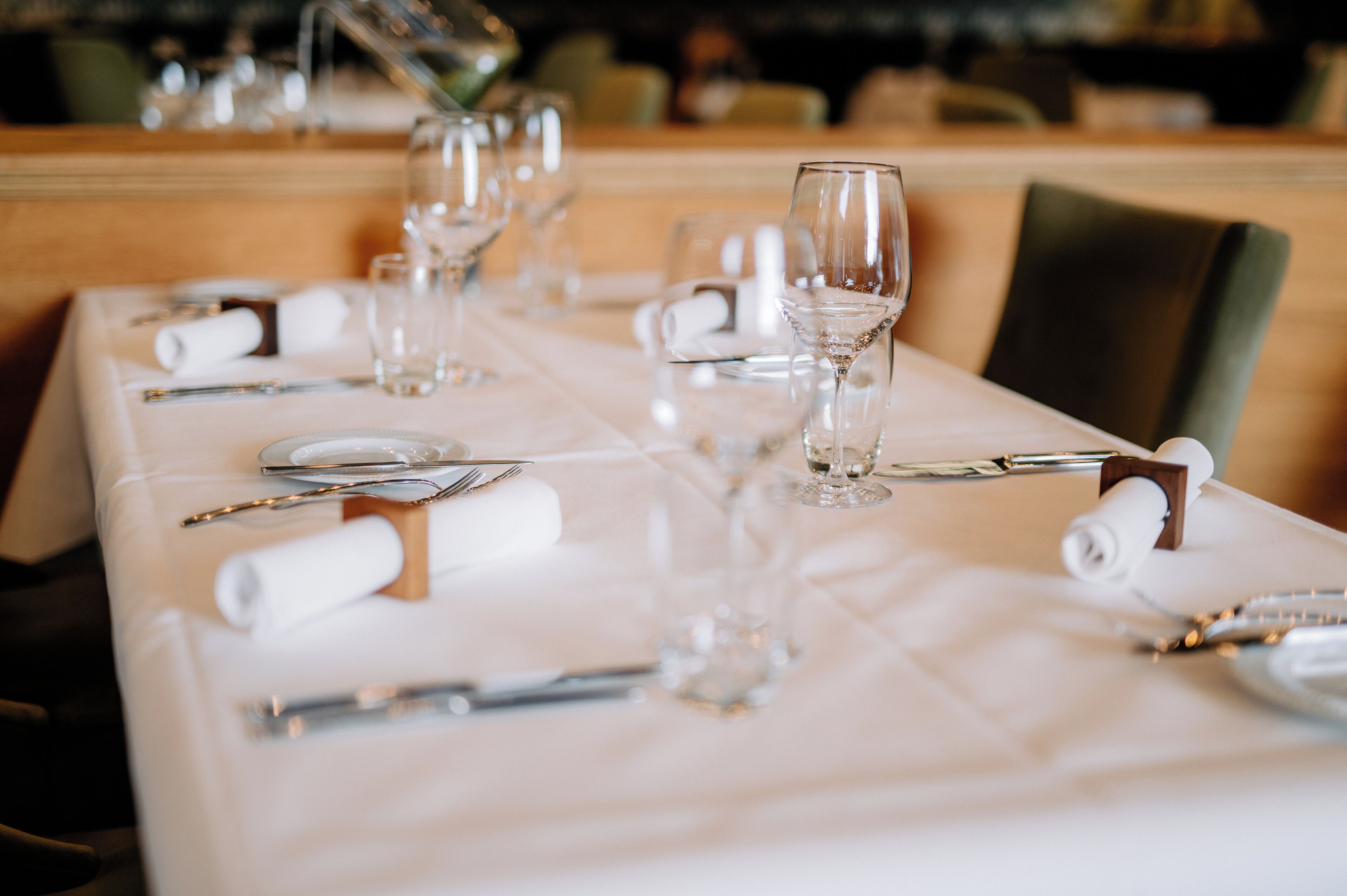 Una mesa de comedor impecablemente dispuesta, con mantel blanco, cubiertos y copas de vino.