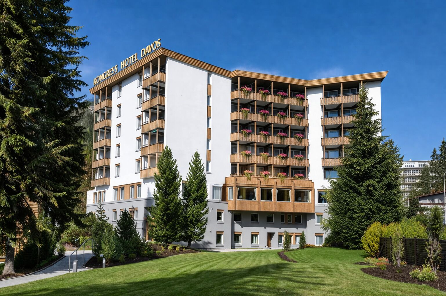 A multi-story hotel with balconies, a well-maintained lawn, and surrounding greenery.