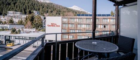 A balcony with a table and chairs overlooking a hotel named Garden Inn, with a mountain view in the background.