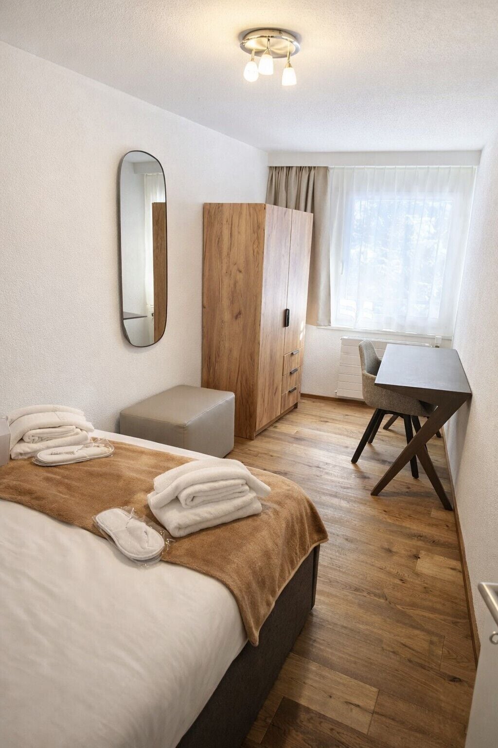 Ett hotellrum med en säng, ett skrivbord, en garderob och en spegel.