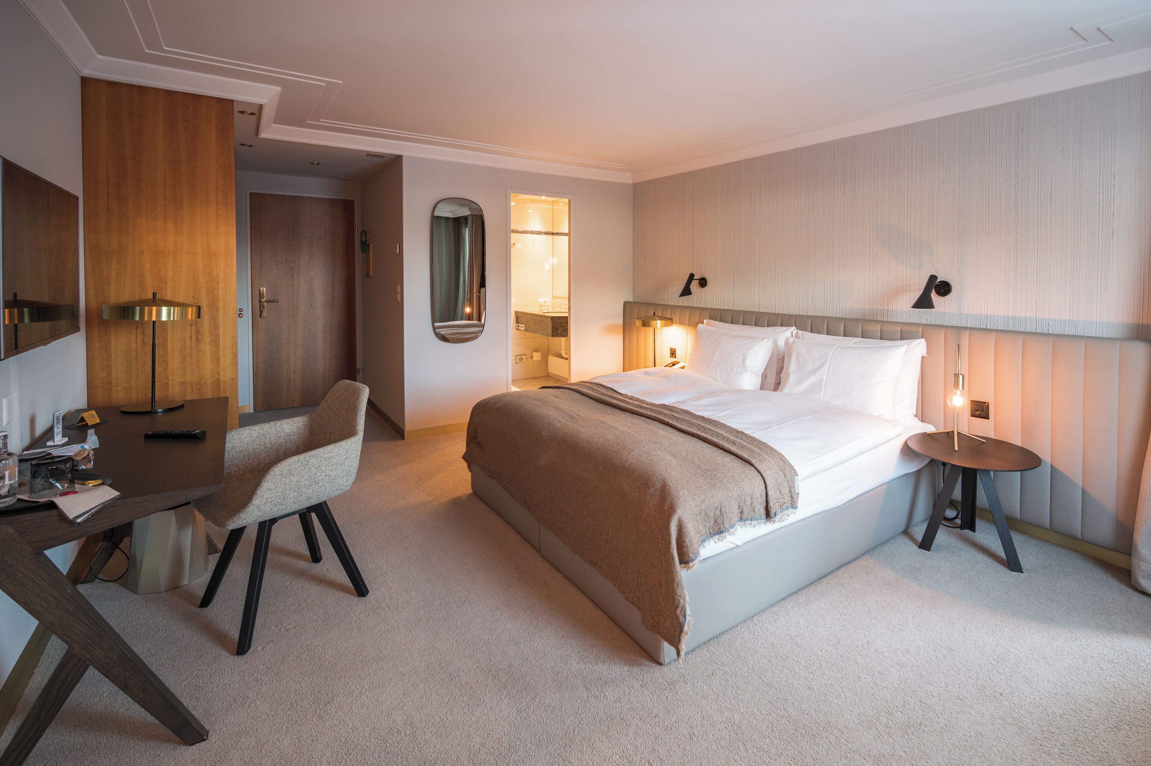 Ein Hotelzimmer mit Bett, Nachttisch, Schreibtisch, Stuhl und Spiegel.