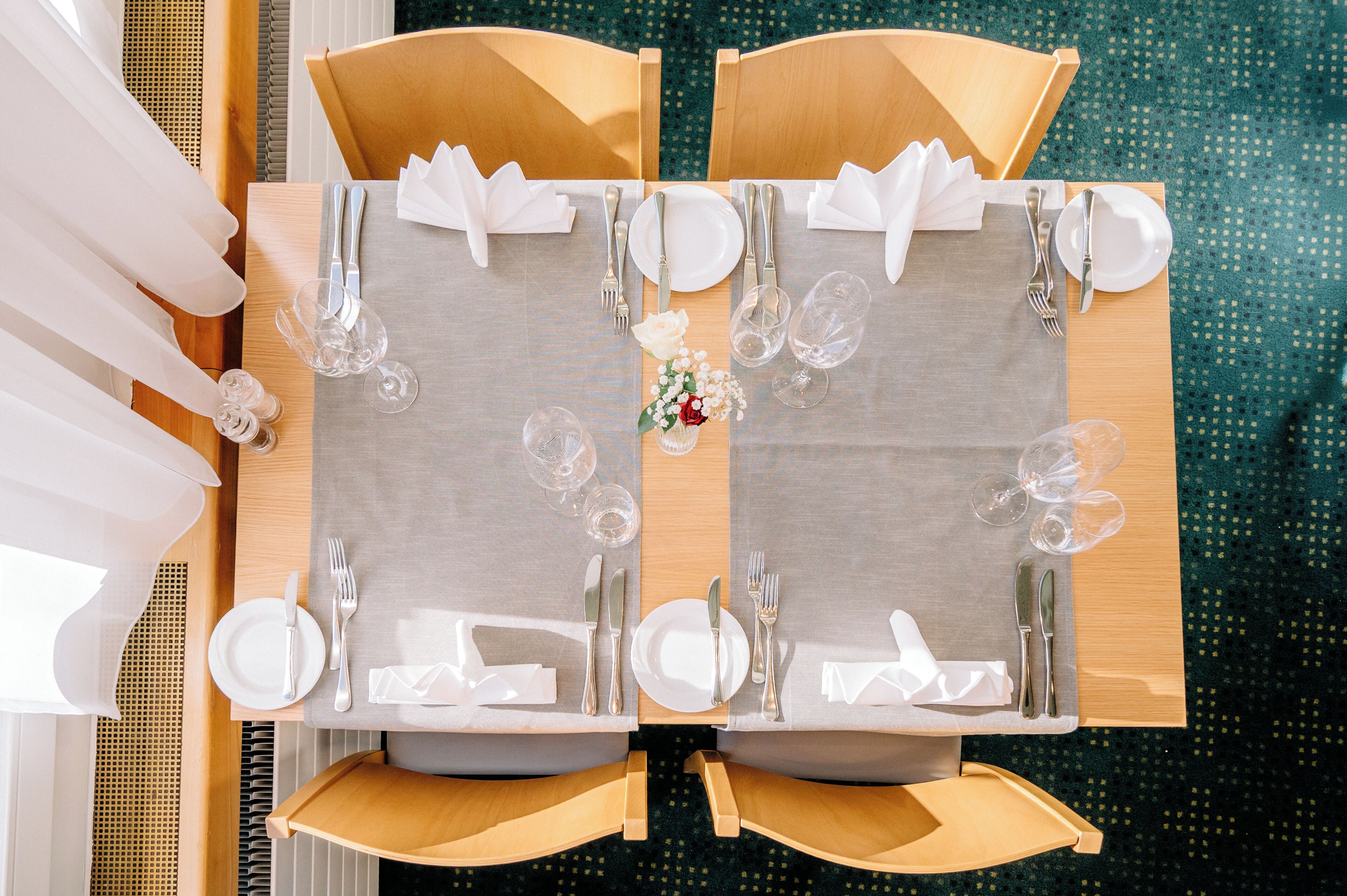 A dining table set for two with white tablecloths, silverware, and clear glasses.