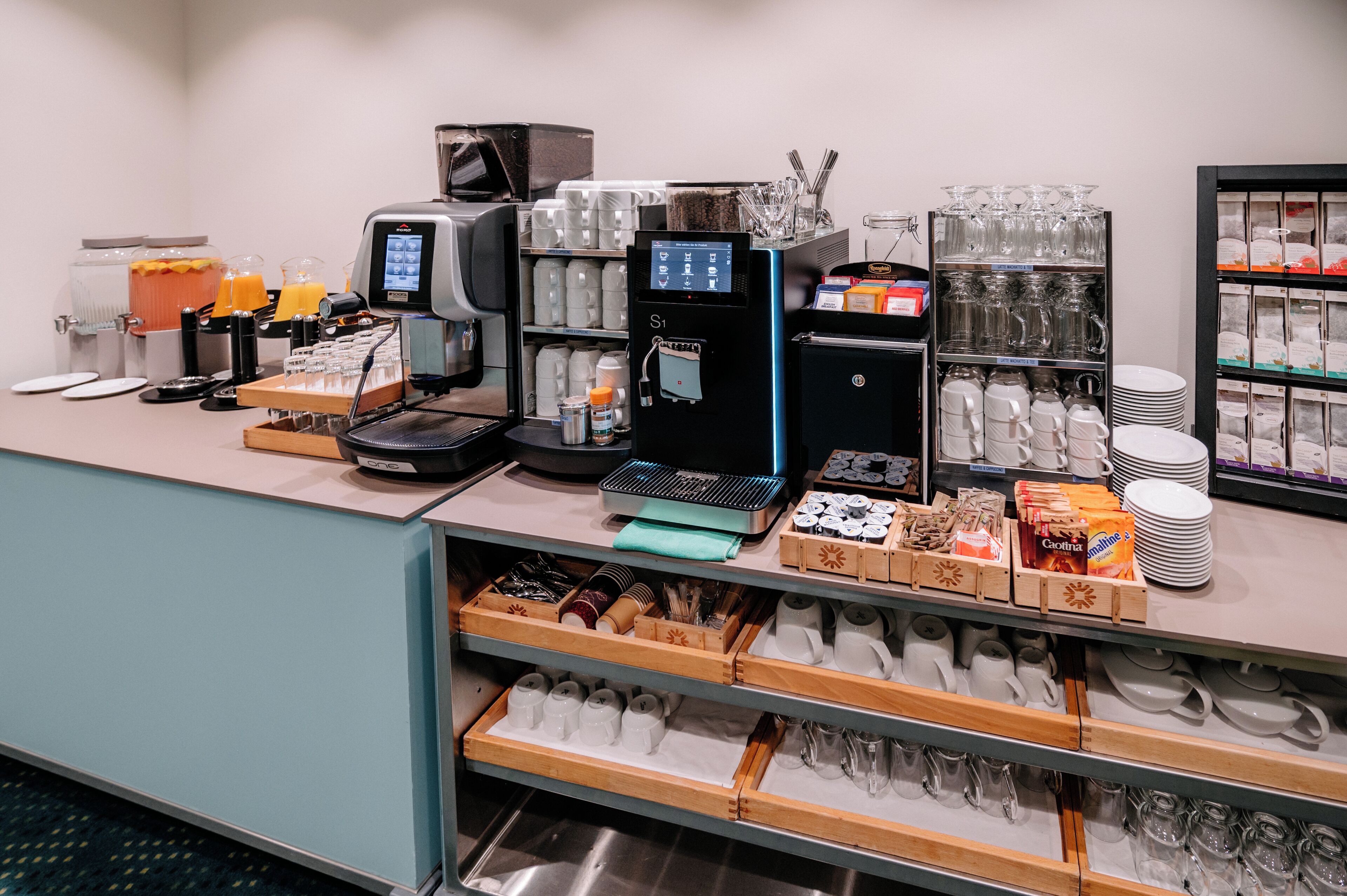 Un espace dédié au café, équipé de plusieurs machines à café, d’un distributeur de jus et d’une variété de récipients pour le café et le thé.