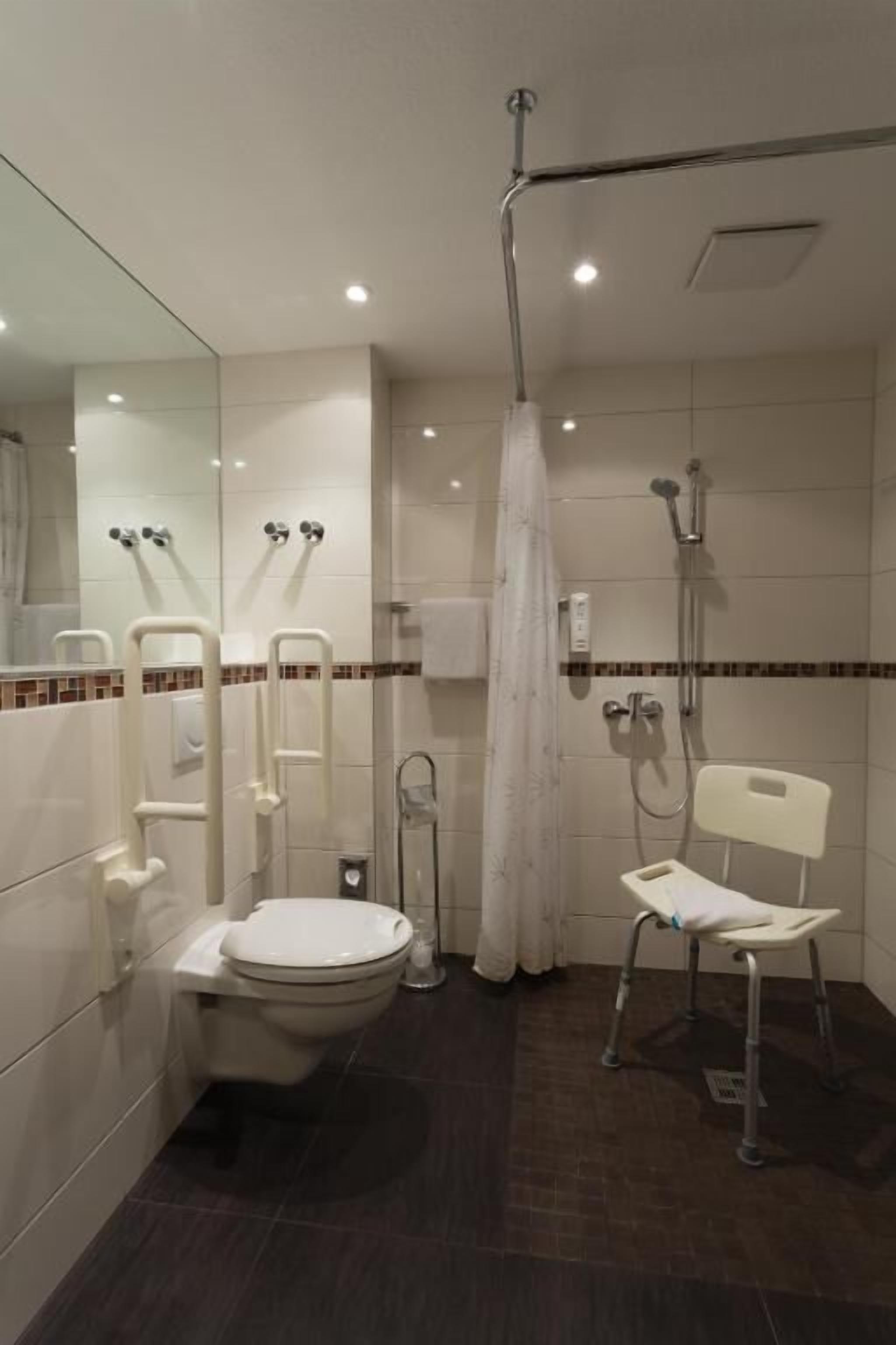 Un bagno moderno con toilette, bidet, doccia e una sedia accessibile per carrozzina.