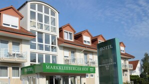 Ein Hotelgebäude mit zahlreichen Fenstern, Balkonen und einem auffälligen, grünen Schild mit der Aufschrift 'Markkleeberger Hof'.