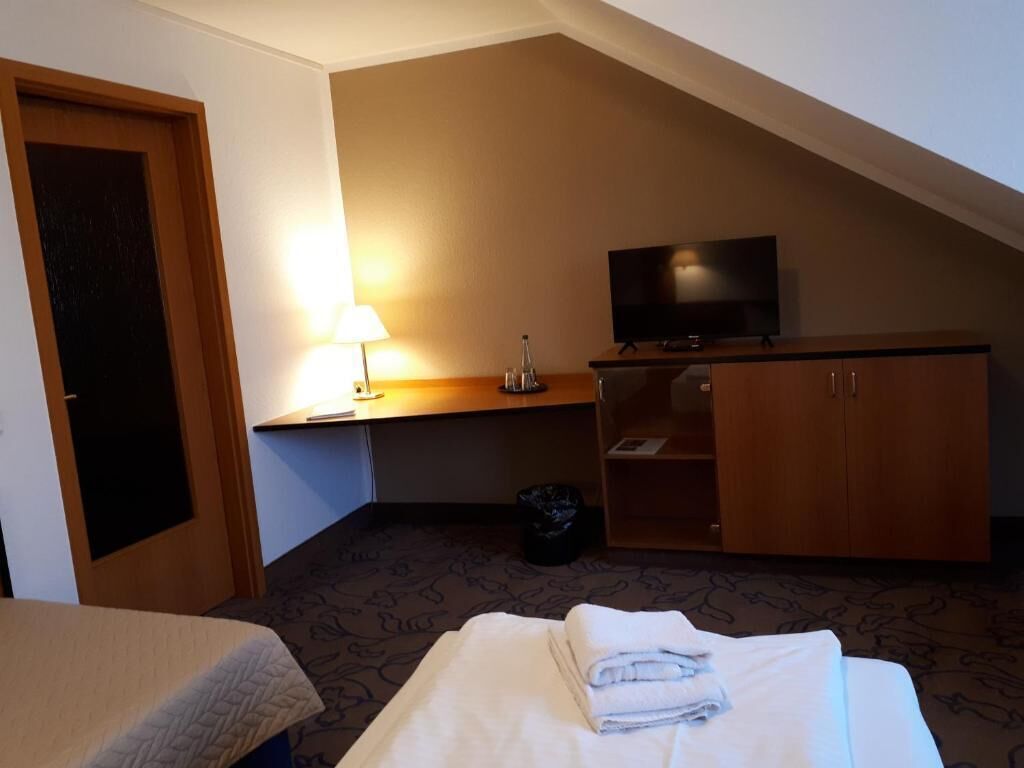 Una habitación de hotel con una cama, un escritorio con lámpara, televisión y armario.