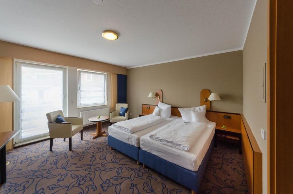 Ein Hotelzimmer mit zwei Betten, einem Schreibtisch, einem Stuhl und einem kleinen Tisch.
