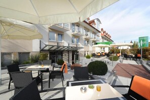 Un espacio al aire libre con mesas, sillas, sombrillas y un edificio con balcones.