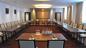 Ein Konferenzraum mit einem langen Tisch, Stühlen, einer Projektionsleinwand und einem großen Fenster.