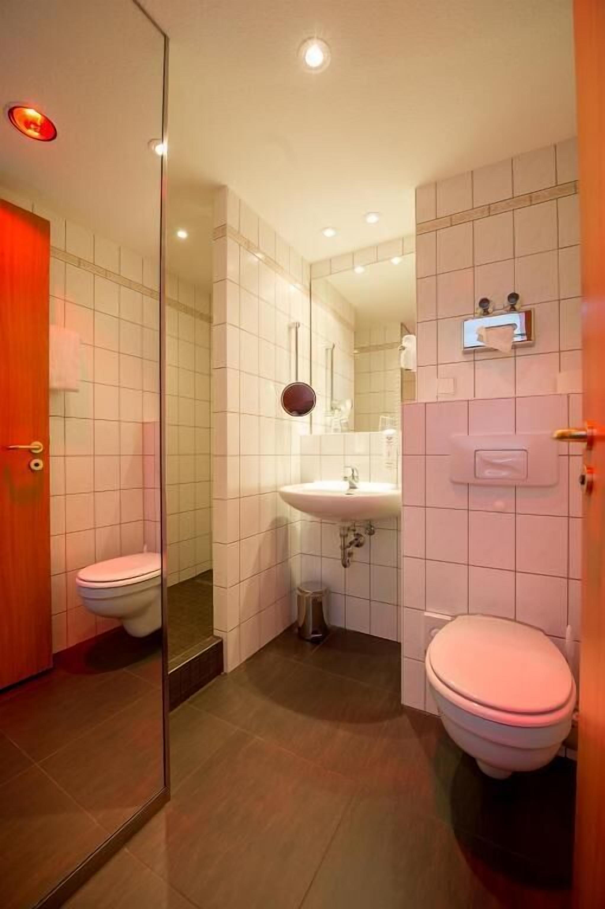 Un baño moderno con mampara de vidrio, inodoro blanco, lavamanos y espejo.
