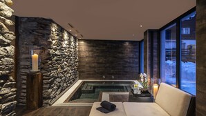 A spa area with a stone wall, a hot tub, a cushioned bench, and a candle. - Unique Hotel Post (Zermatt)
