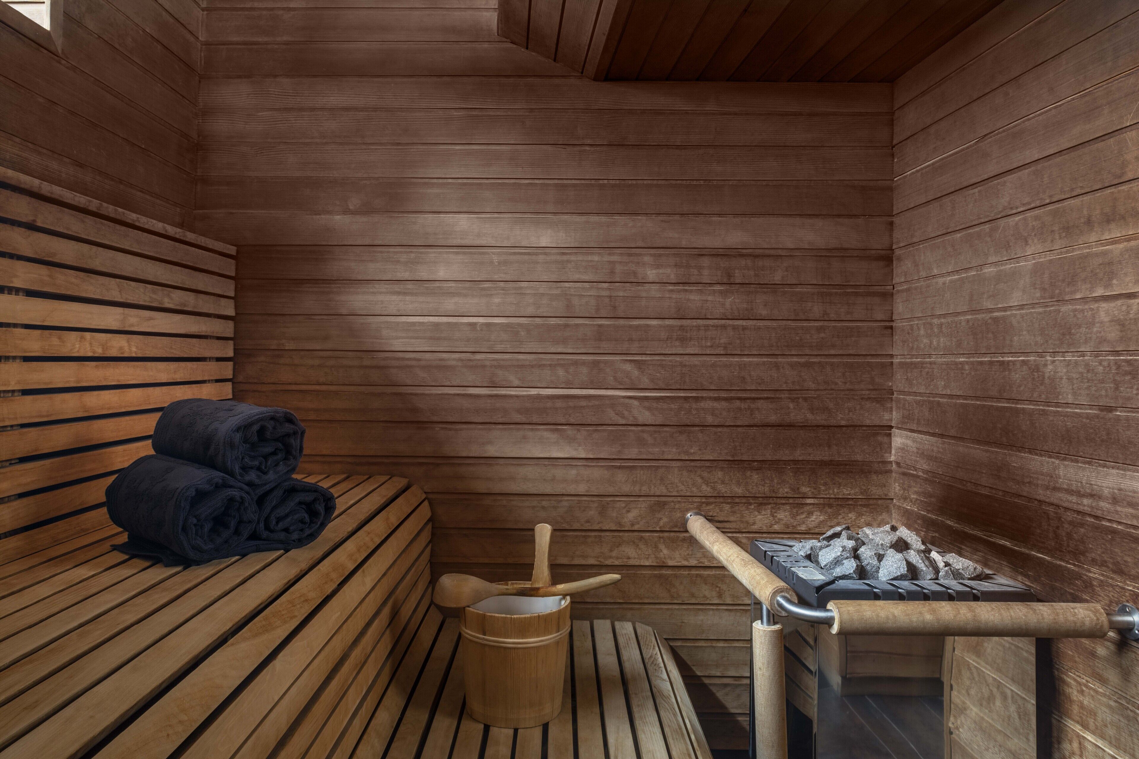 A sauna with wooden benches, a wooden bucket, and a stone heater.