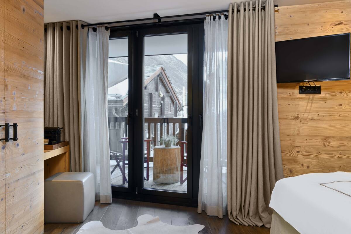 A modern room with a sliding glass door leading to a balcony, wooden walls, a flat-screen TV, and a cozy seating area with a small table and chairs.