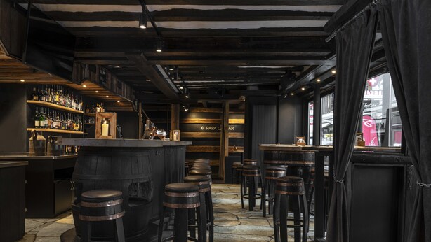 A bar area with stools, a bar counter, and shelves of bottles. - Unique Hotel Post (Zermatt)