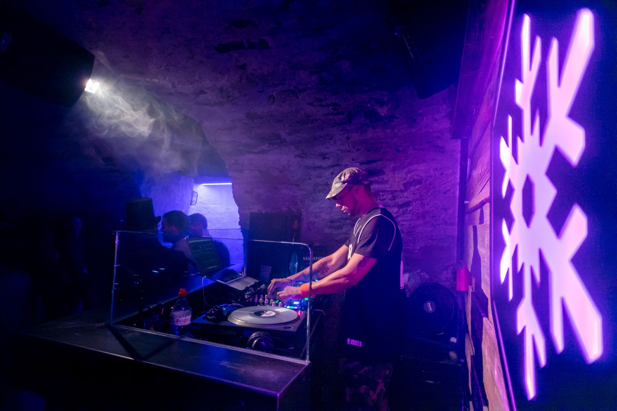 Piso de DJ com um laptop, toca-discos e uma garrafa de água Evian.