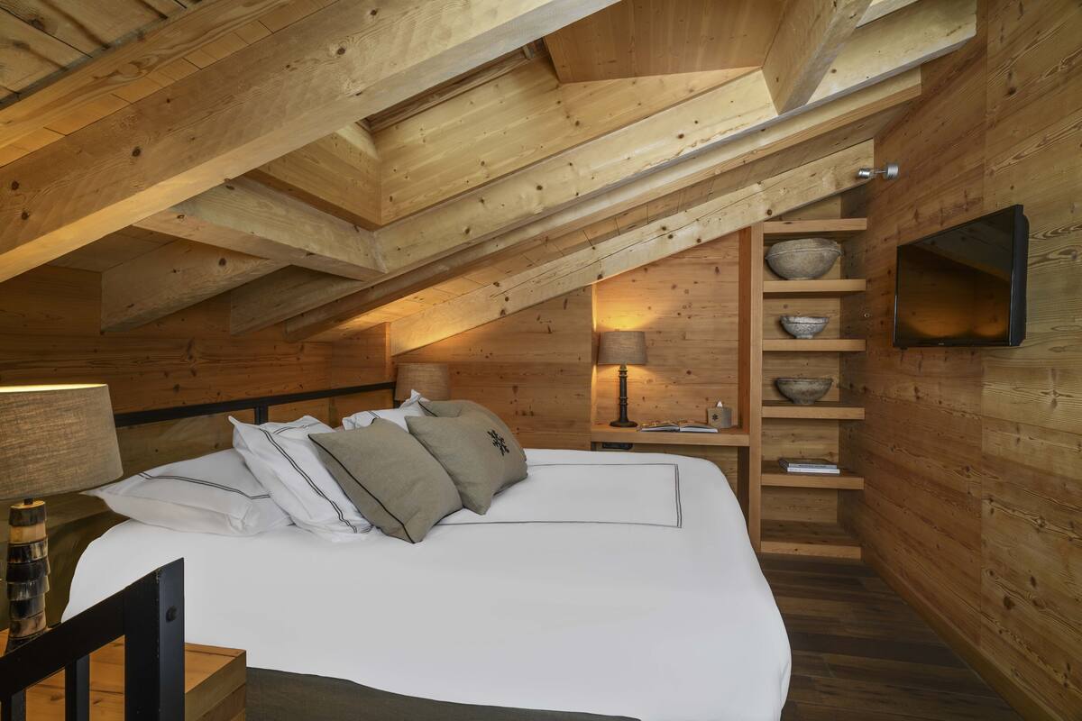 A wooden interior with a bed, shelves, and a television.