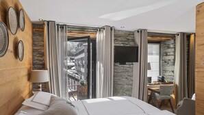 A hotel room with a bed, a desk with a chair, a TV, and a stone wall. - Unique Hotel Post (Zermatt)