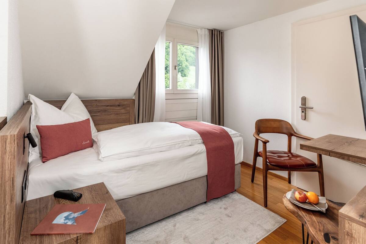 Une chambre à coucher avec un lit, un bureau, une chaise et une fenêtre avec des rideaux.