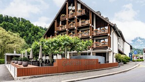 Ein mehrstöckiges Gebäude mit Balkonen, einem Schild mit der Aufschrift 'Garten Lounge' und Außenbestuhlung mit Sonnenschirmen.