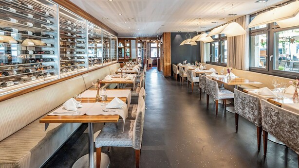 Ein Restaurant mit einer langen Theke, mehreren Tischen und einem Weinkühlschrank links.