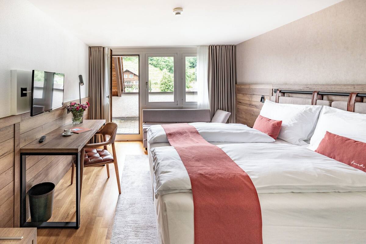 Une chambre d’hôtel équipée d’un lit, d’un bureau, d’une chaise, d’une télévision et offrant une vue sur l’extérieur.