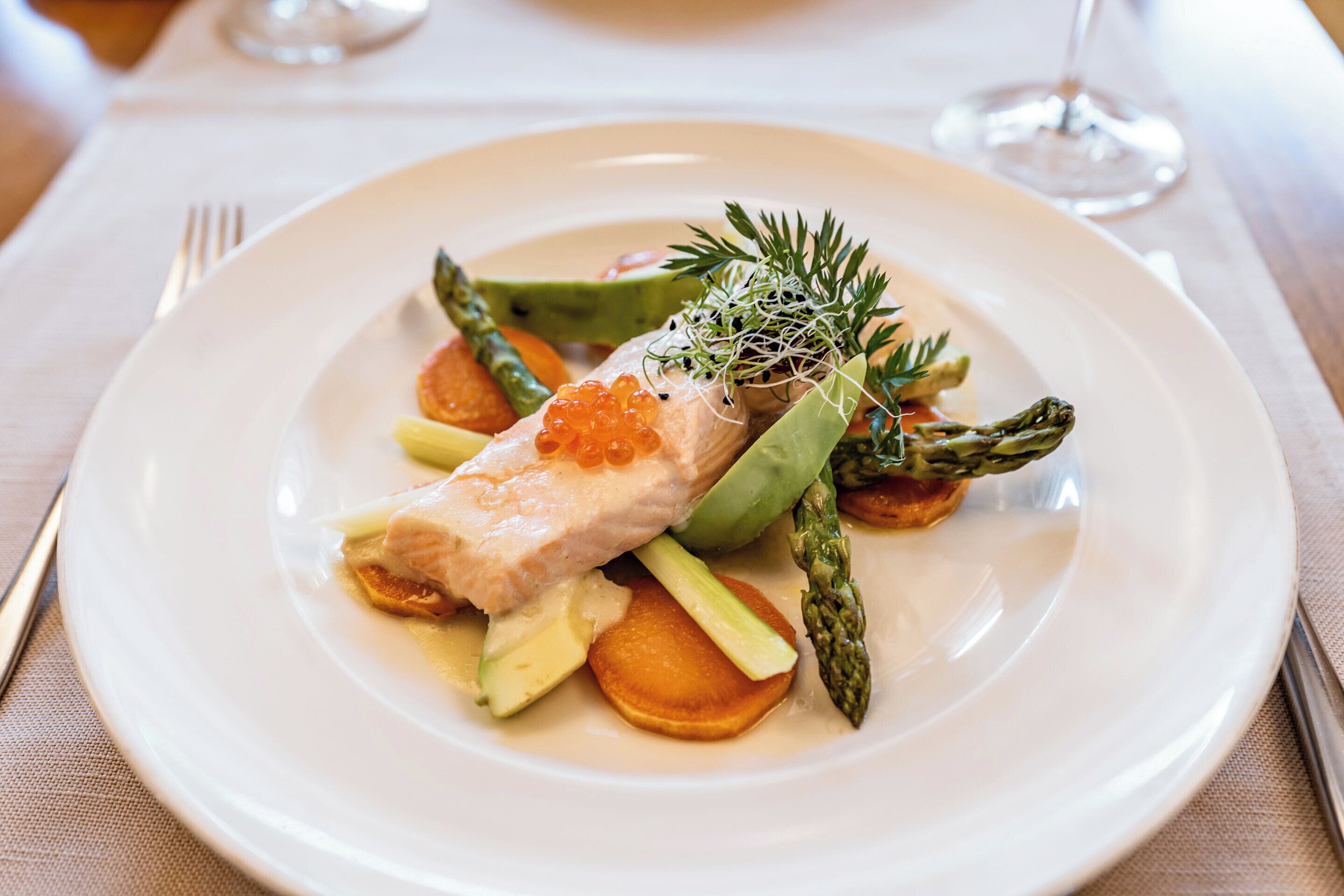 Une assiette blanche garnie de saumon, d’asperges, d’herbes fraîches et de jeunes pousses.