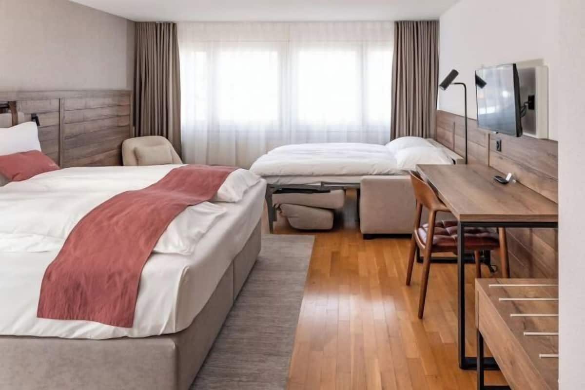 Une chambre d’hôtel avec deux lits, un bureau, une chaise, une télévision et une fenêtre avec des rideaux.