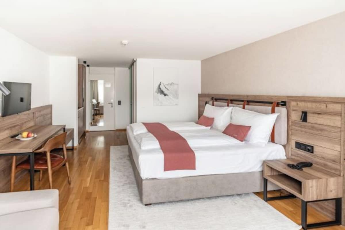 A modern hotel room with a bed, bedside table, desk, and chair.