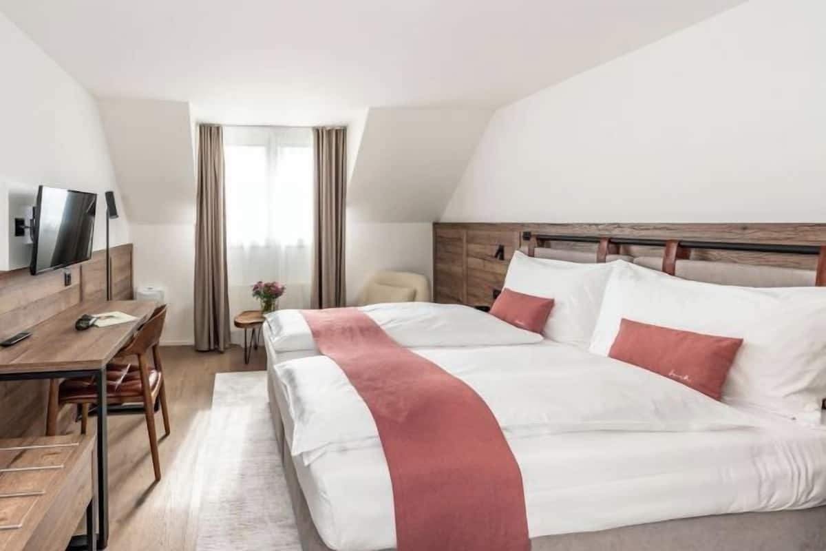 Une chambre d’hôtel avec un lit, un bureau, une chaise, une télévision et une fenêtre avec des rideaux.