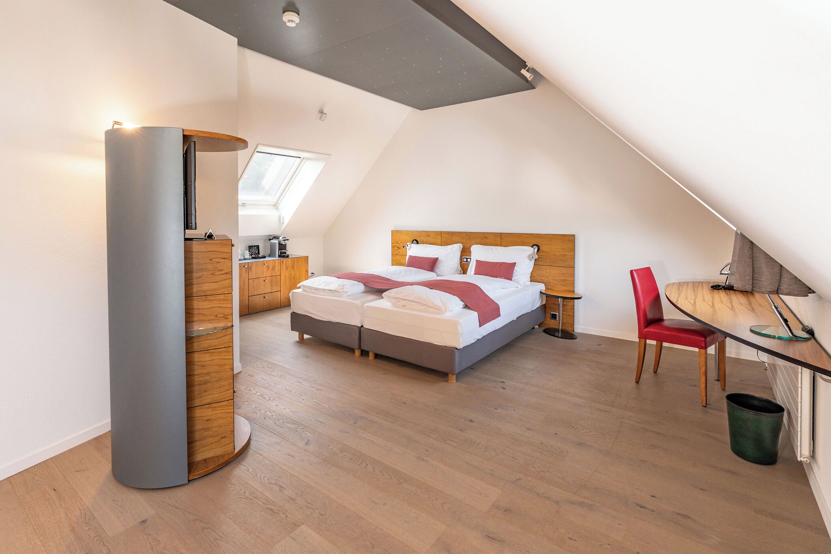Un dormitorio moderno con techo estilo loft, una cama con cabecera de madera, una silla roja y un escritorio con lámpara.