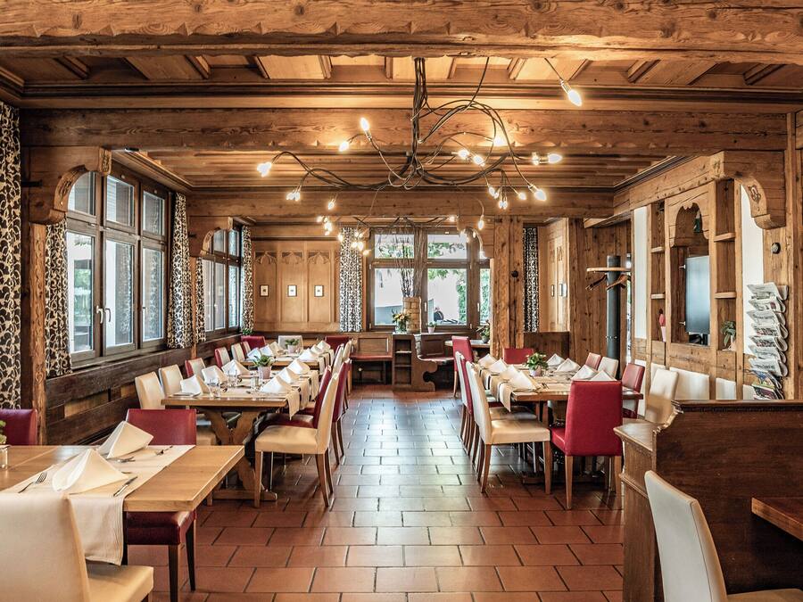 A restaurant with wooden interiors, multiple tables, and chairs arranged for dining.