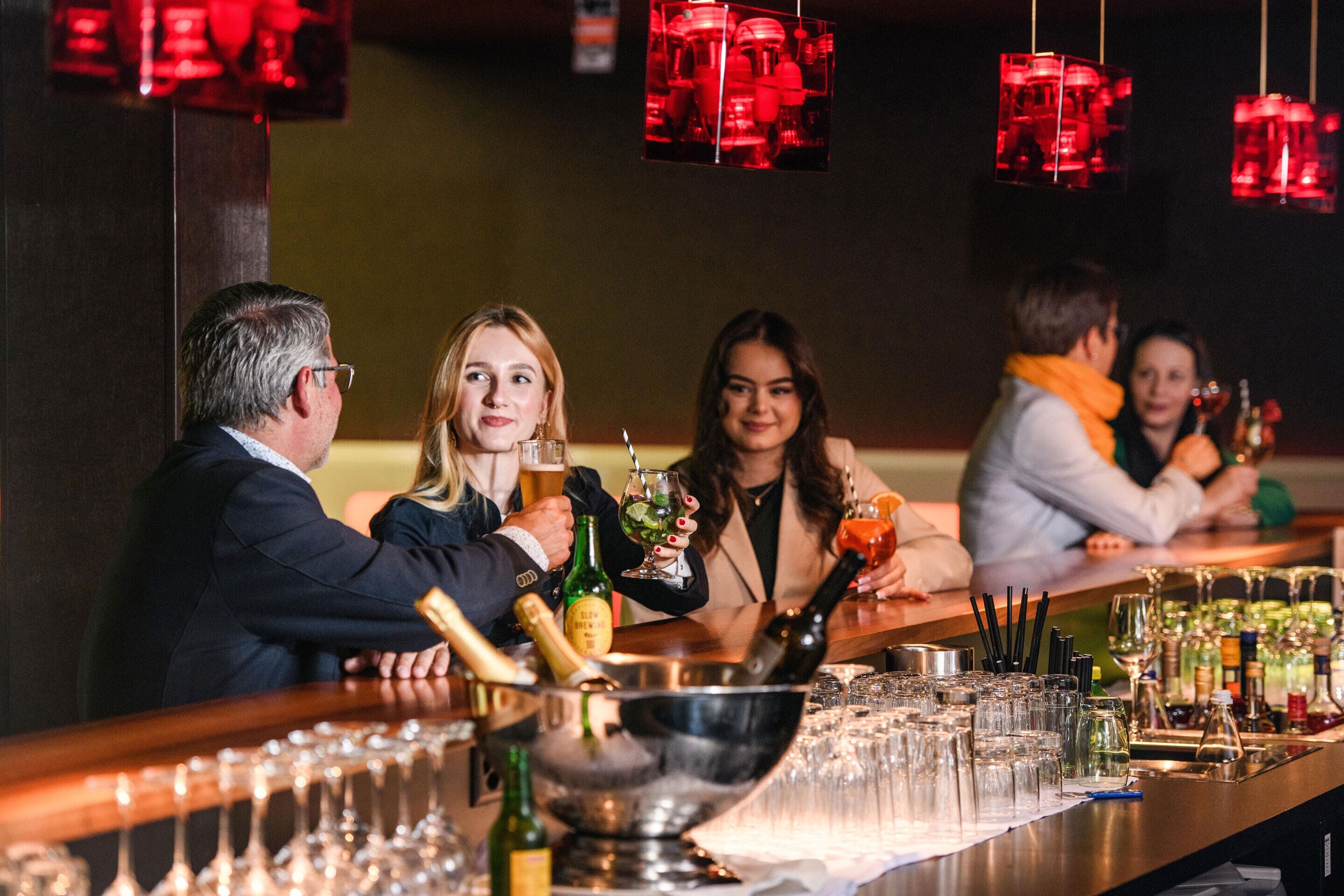 Un espace bar avec un long comptoir, des verres, des bouteilles et un récipient en métal.