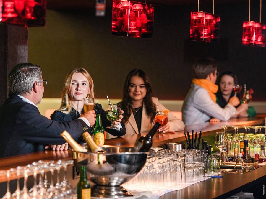 Un espace bar avec un long comptoir, des verres, des bouteilles et un récipient en métal.