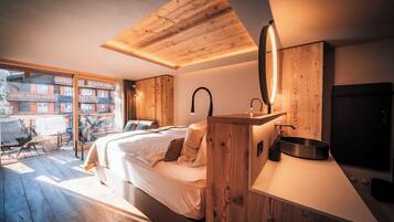 Ein modernes Schlafzimmer mit Holzboden, einem großen Bett, einem Nachttisch mit Spiegel und Blick auf ein Gebäude durch große Fenster.