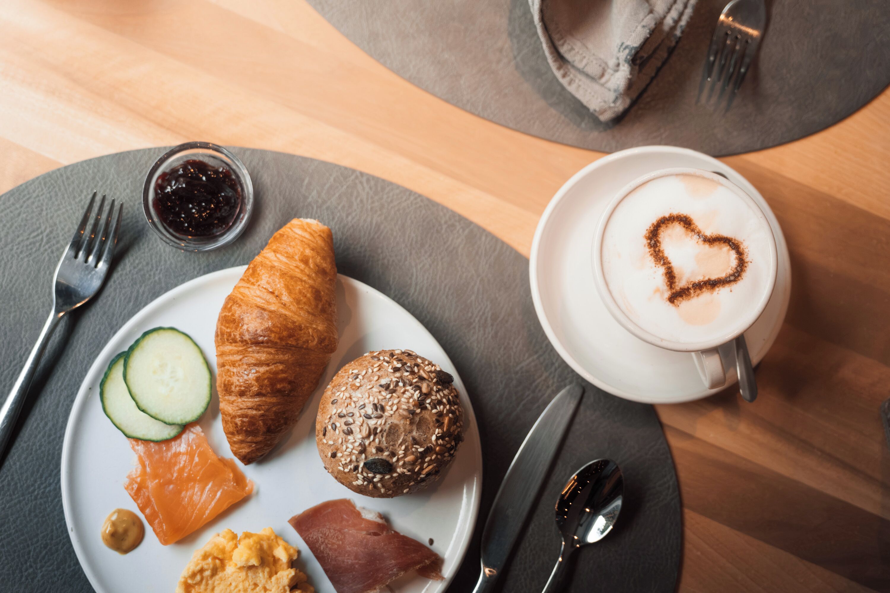 A breakfast setting with croissants, a muffin, smoked salmon, and a cup of coffee with a heart-shaped latte art.