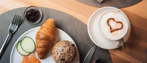 A breakfast setting with croissants, a muffin, smoked salmon, and a cup of coffee with a heart-shaped latte art.