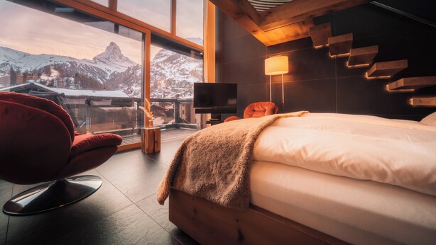 Ein modernes Hotelzimmer mit großem Fenster, einem Bett, einem Fernseher und einem roten Sessel.