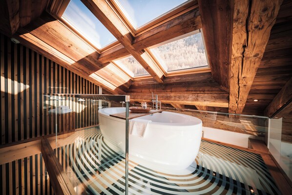 A modern bathroom with a freestanding bathtub, skylights, and a wooden ceiling. - Hotel Bellerive (Zermatt)