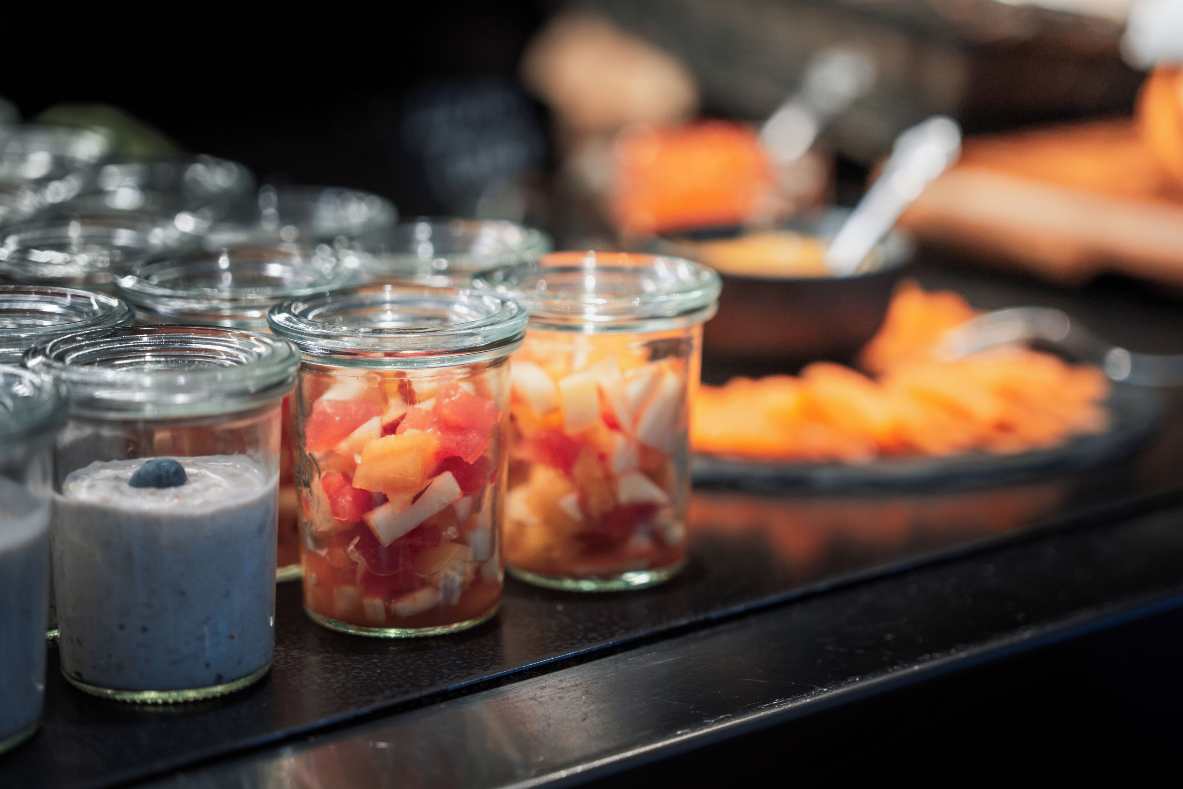 Uma mesa de buffet com diversos alimentos em recipientes de vidro.
