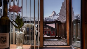 Ein Zimmer mit großem Fenster mit Blick auf einen verschneiten Berg und ein rotes Gebäude.