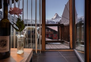 Una habitación con un amplio ventanal que da a una montaña nevada y un edificio rojo.
