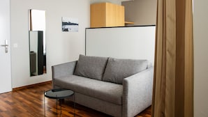A modern living room with a grey sofa, a small black side table, a wooden cabinet, and a mirror on the wall. - Royal Hotel (Basel)