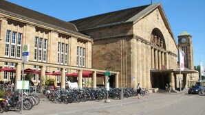 A historic building with a large clock tower, a covered outdoor seating area, and a bike parking area. - Royal Hotel (Basel)