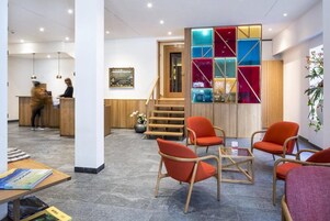 Un vestíbulo de hotel con mostrador de recepción, zona de estar, escalera y una decoración de pared colorida.