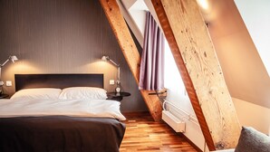 A bedroom with a wooden ceiling, a bed with white linens, two bedside lamps, and a nightstand. - Royal Hotel (Basel)